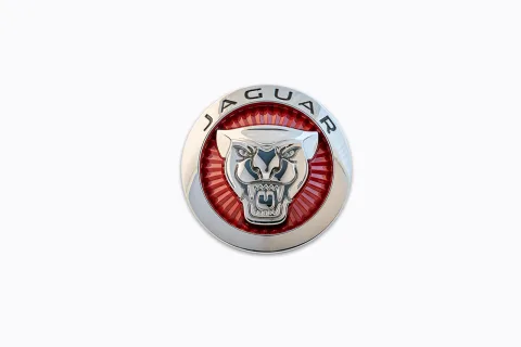 Emblema Jaguar cromado, com anel vermelho e cabeça de jaguar em relevo